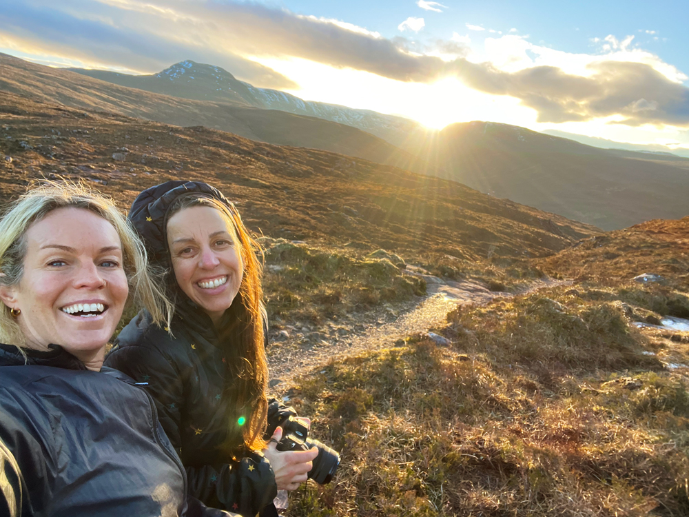 Two women walking in the Scottish Highlands surrounded by mountains and changing weather